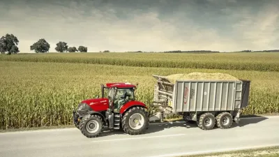 Červený traktor Case IH Puma veze přívěs s nákladem po silnici u pole.