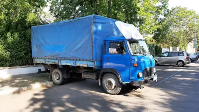 Modrý nákladní automobil AVIA s plachtovou nástavbou u stromů.