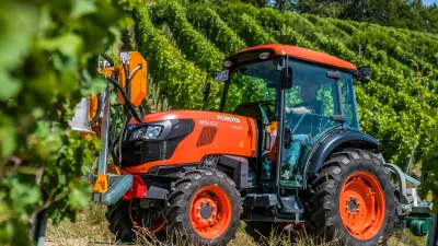 Oranžový úzkorozchodný traktor Kubota ve vinici.