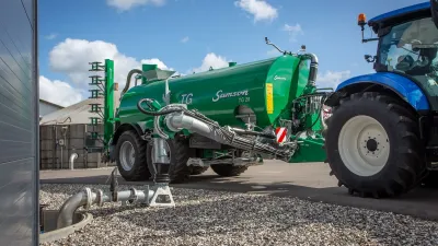Zelená cisterna Samson připojená k modrému traktoru.