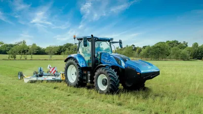 Modrý traktor New Holland Methane Power při sečení louky.