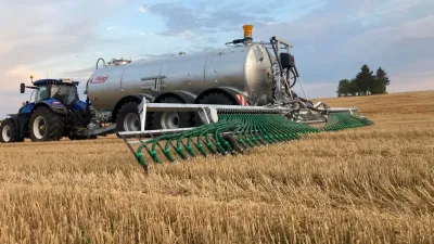 Traktor táhne cisternu s botkovým aplikátorem Fliegl po poli.