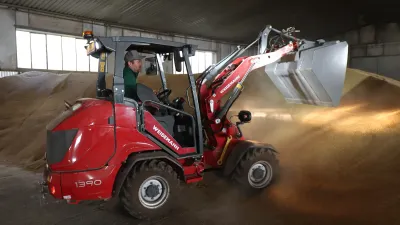 Červený nakladač Weidemann při manipulaci s materiálem ve skladu.
