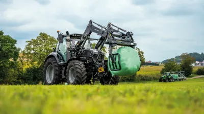 Traktor Deutz-Fahr s kulatým balíkem v předním nakladači.
