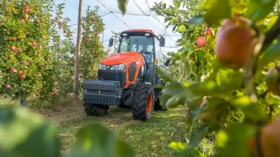 Oranžový úzkorozchodný traktor Kubota v jabloňovém sadu.
