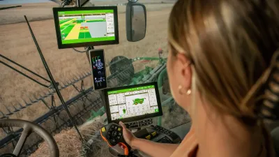 Řidička sleduje monitory John Deere v kabině stroje.