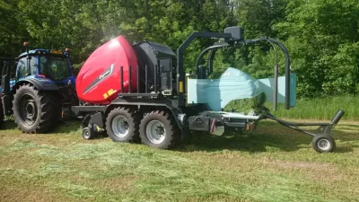 Traktor s lisem Kverneland a ovinutým kulatým balíkem na louce.