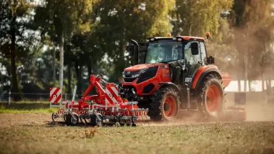Oranžový traktor Kioti s nářadím na poli.