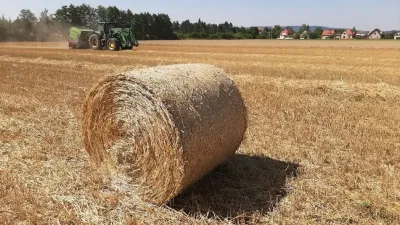 Kulatý balík slámy na poli se strojem v pozadí