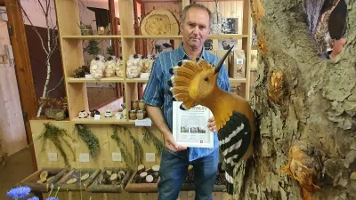 Muž s listinou stojí vedle modelu ptáka a stromu