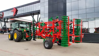 Traktor s červenozeleným kypřičem AGRO-MASZ před budovou