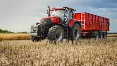 Červený traktor s červeným zemědělským návěsem na poli