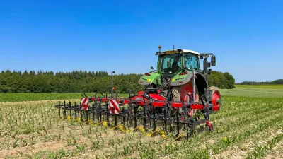 Zelený traktor s meziřádkovým kultivátorem na poli s mladou kukuřicí