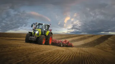 Traktor Claas s podmítačem na poli za soumraku