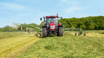 Červený traktor s rozloženým shrnovačem Krone Swadro na louce