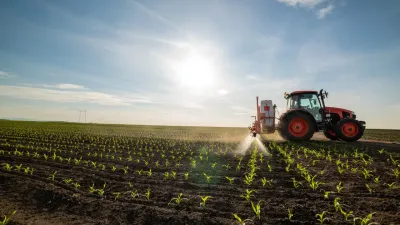 Traktor s postřikovačem ošetřuje mladý porost na poli