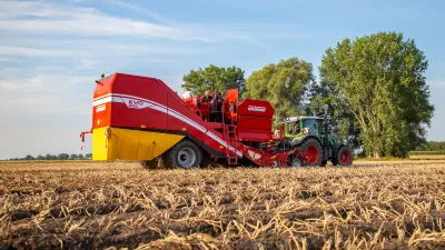 Červený sklízeč brambor Grimme EVO 260 s traktorem na poli