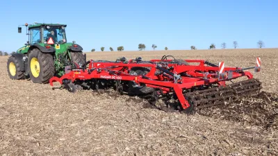 Zelený traktor John Deere s červeným kypřičem SMS CZ Finisher na poli