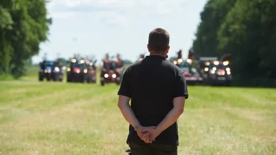 Muž stojí zády k fotografovi před řadou zemědělských strojů