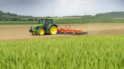 Zelený traktor táhne červené prutové brány Pöttinger po poli