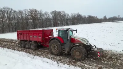 Traktor Steyr s červeným přívěsem na zasněženém poli