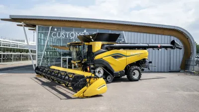Žlutá sklízecí mlátička New Holland CR10 před budovou.