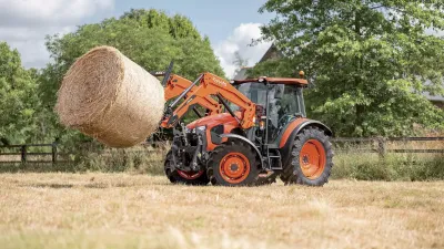 Oranžový traktor Kubota zvedá balík sena.