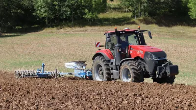Červený traktor Case IH Magnum s pluhem při orbě pole.