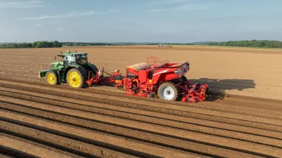 Traktor táhne červený sazeč brambor Grimme po poli.