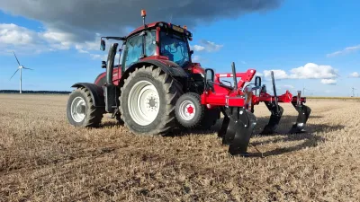 Traktor s červeným kypřičem SMS CZ na poli.