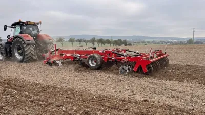 Traktor s červeným strojem SMS CZ při práci na poli.