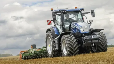 Modrý traktor New Holland na poli pod zamračenou oblohou