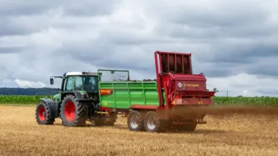 Traktor táhne zelené rozmetadlo Strautmann po poli