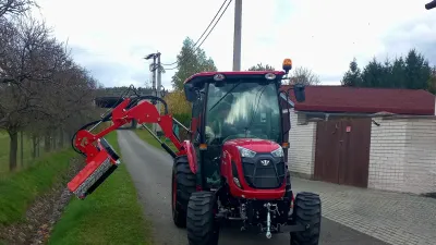 Červený traktor TYM s ramenovou sekačkou u silnice