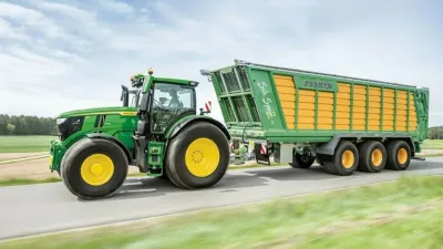 Zelený traktor John Deere s návěsem na louce
