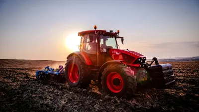 Červený traktor při práci na poli za západu slunce
