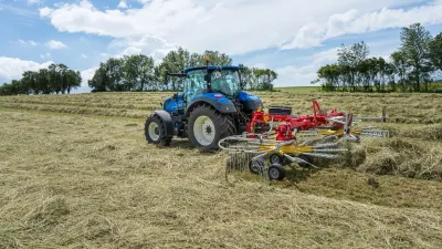 Modrý traktor se shrnovačem sena na louce