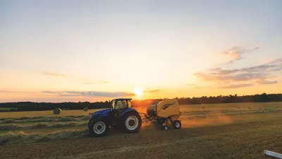 Modrý traktor s lisem při práci na poli za západu slunce