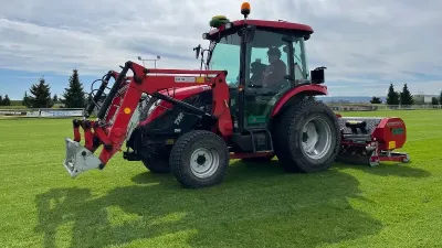 Červený traktor TYM s čelním nakladačem na travnaté ploše