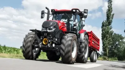 Červený traktor Case IH Maxxum 145 táhnoucí návěs po silnici.