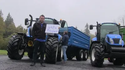 Muž stojí před modrými traktory New Holland