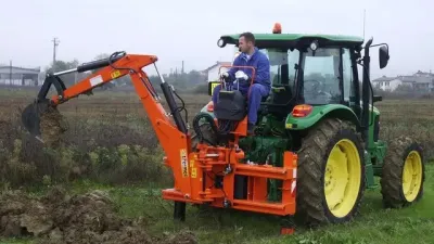 Oranžové rýpadlo Vogt namontované na zeleném traktoru při výkopových pracích.