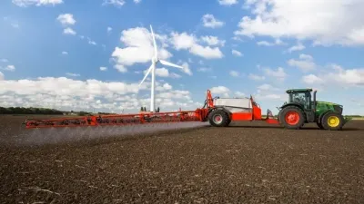 Traktor táhne červený postřikovač přes pole
