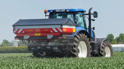 Modrý traktor s rozmetadlem Vicon při aplikaci hnojiva na poli