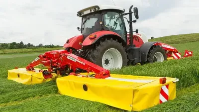 Červený traktor se žacím strojem Pöttinger Novacat na louce