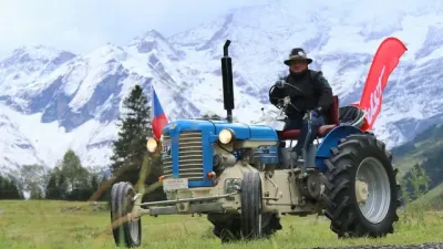 Řidič na modrém historickém traktoru Zetor 25 před zasněženými horami