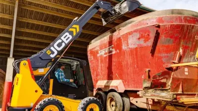 Žlutý smykem řízený nakladač JCB nakládající krmný vůz