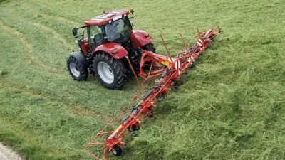 Červený traktor s širokým obracečem Kuhn při práci na louce