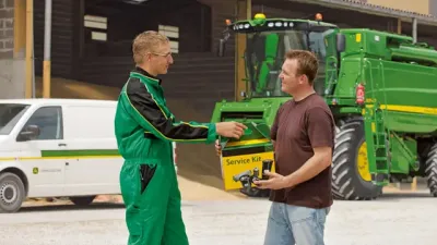Servisní technik si podává ruku s farmářem před kombajnem John Deere