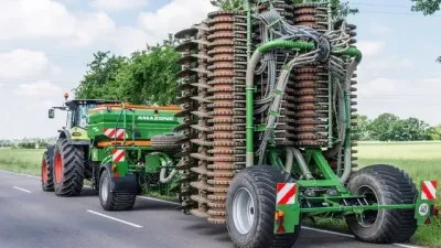Traktor táhne složený zelený secí stroj Amazone po silnici